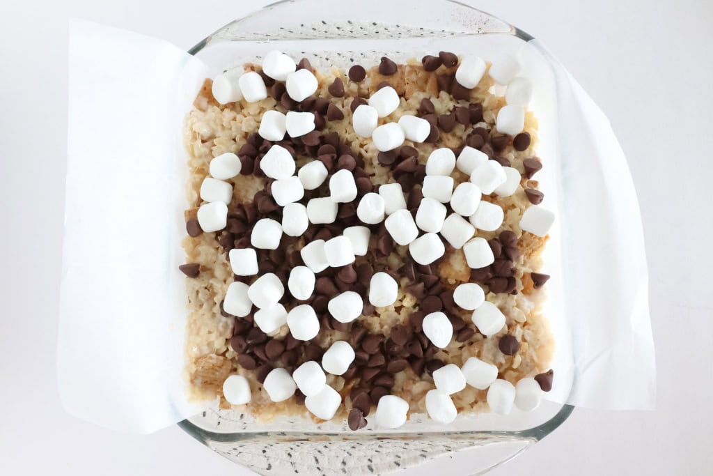 Mixed ingredients of S'mores Rice Krispies pressed into baking dish topped with chocolate chips and marshmallows
