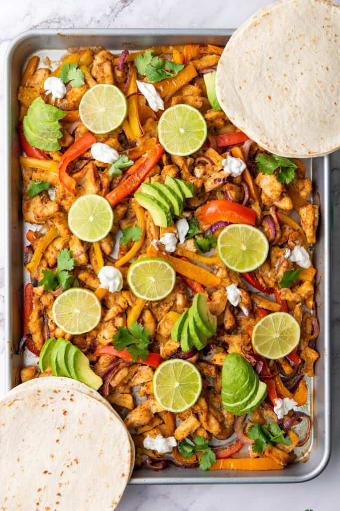 Sheet Pan Chicken Fajitas topped with avocado and lime slices, dollops of sour cream