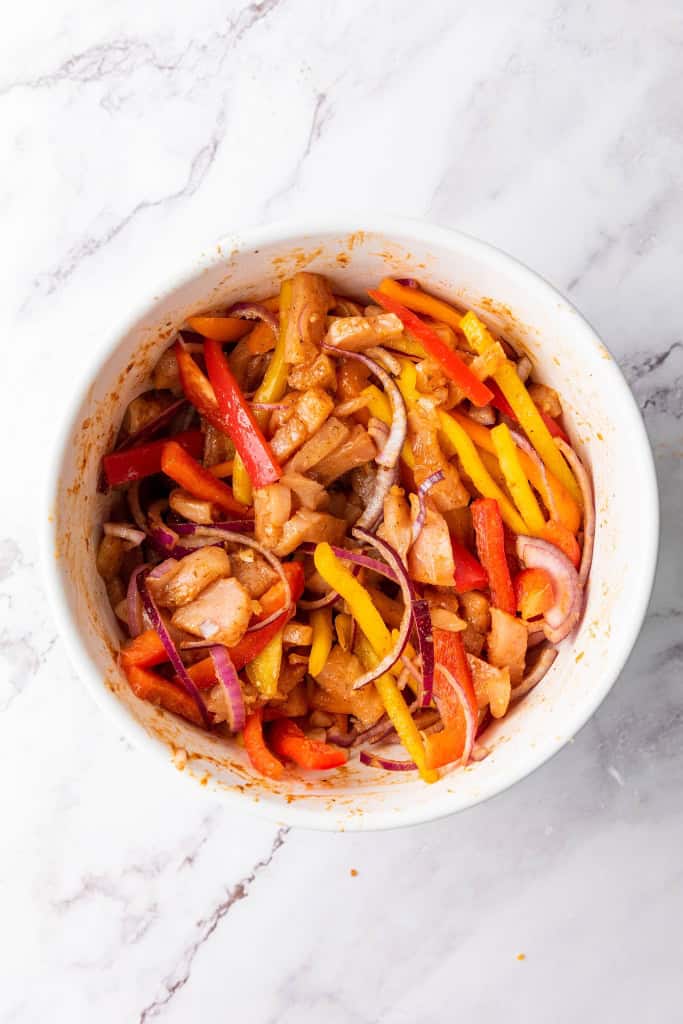 mixing the ingredients of Sheet Pan Chicken Fajitas in a bowl