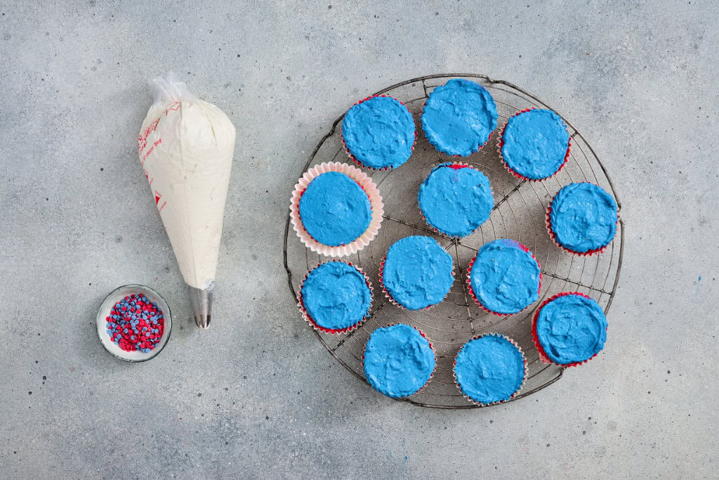 cream topping in piping bag with assembled cheesecakes in muffin liners